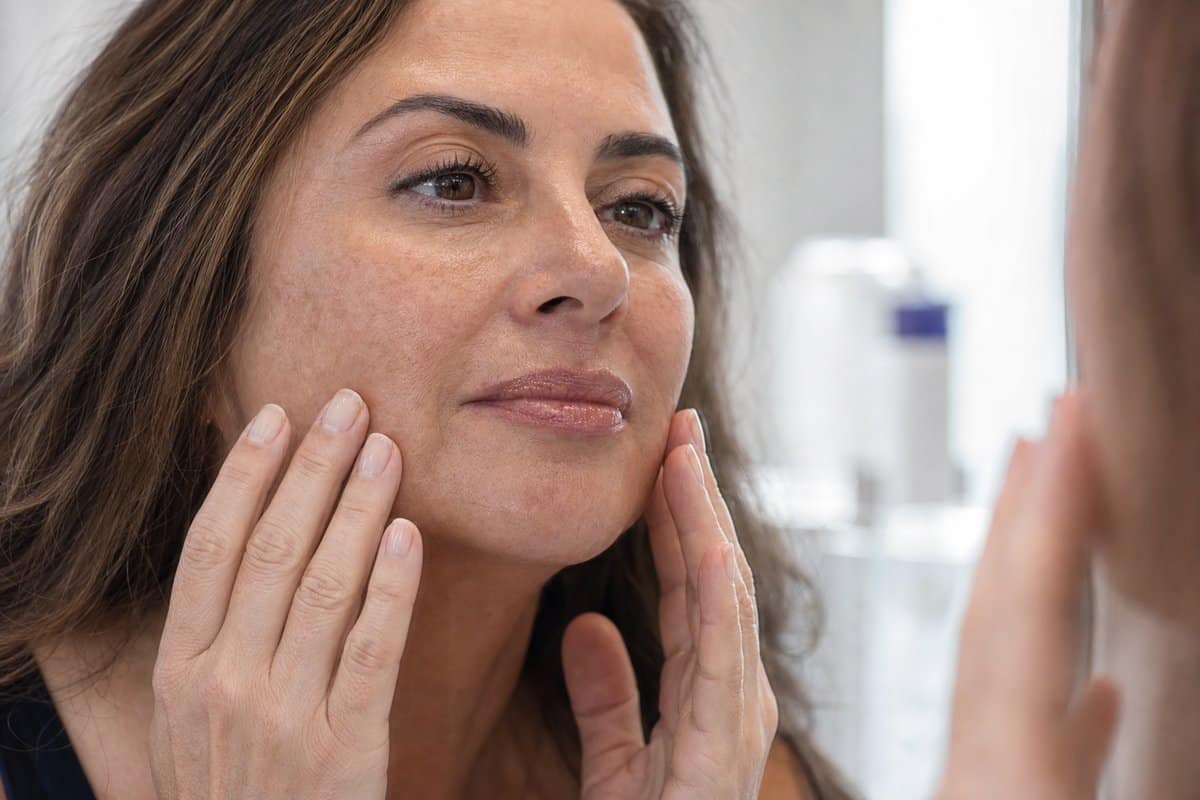 Close-up of a woman's refreshed cheeks at a vanity mirror showing improved acne scar texture after microneedling sessions