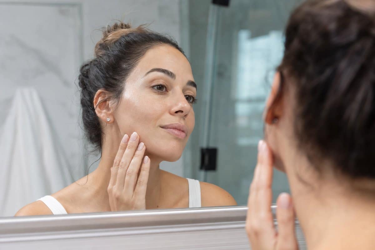 Woman in her 30s admiring her bright, hydrated facial skin in a mirror after an IV drip session