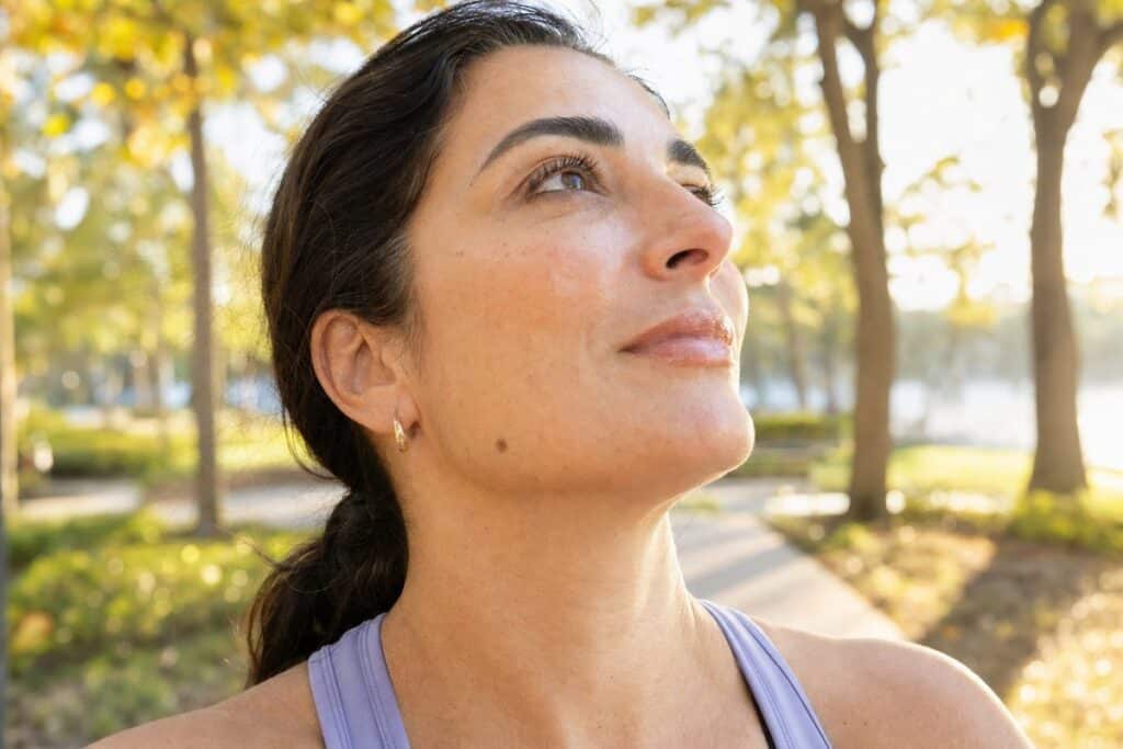 Confident woman with glowing hydrated skin walking through a sunlit Miami Lakes park after IV hydration therapy
