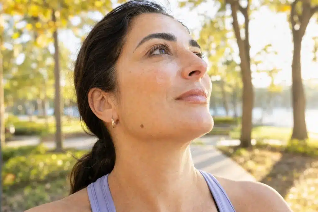 Confident woman with glowing hydrated skin walking through a sunlit Miami Lakes park after IV hydration therapy