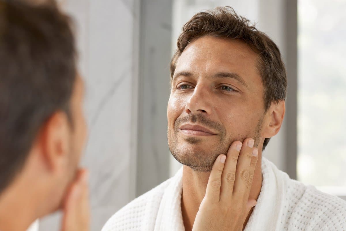 Man in his early 40s touching smooth, refreshed facial skin in a mirror after PRP facial rejuvenation