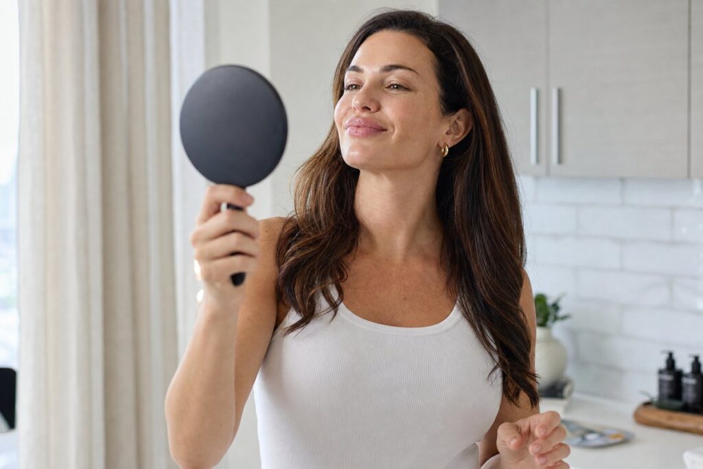 Woman in her late 30s admiring her Botox lip flip result in a handheld mirror at home