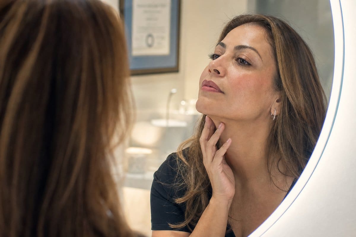 Latina woman in her 40s admiring her slimmer jawline in a vanity mirror after weight loss treatment