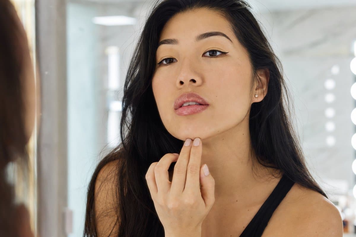 Young woman examining her smooth, natural-looking lips in a mirror after lip filler treatment