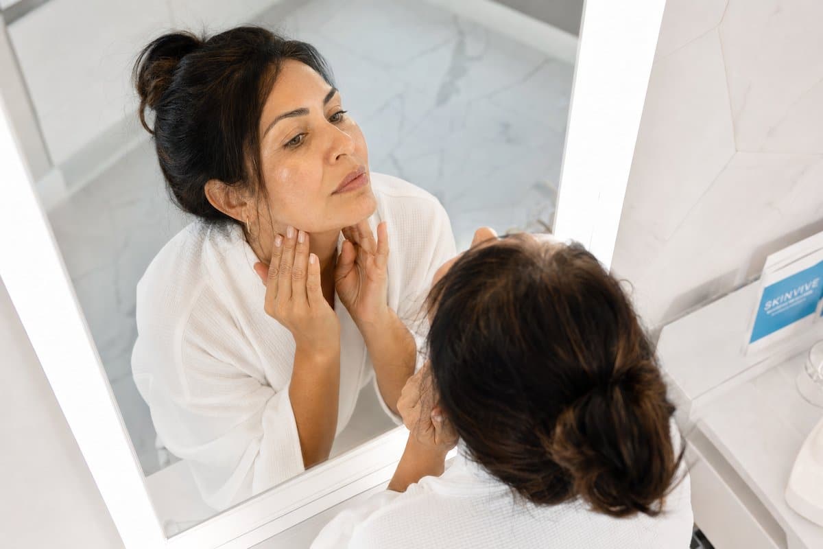 Latina woman in her 40s admiring smooth, hair-free skin along her jawline after laser hair removal