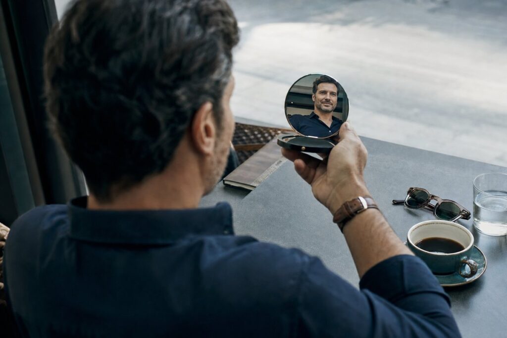 Man in his 40s at a café reviewing his weight loss results in a compact mirror after compounded semaglutide therapy