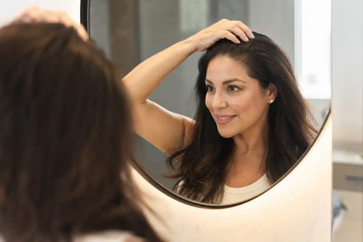 Latina woman in her 40s admiring her full, thick restored hair in a mirror after completing her PRP hair growth schedule