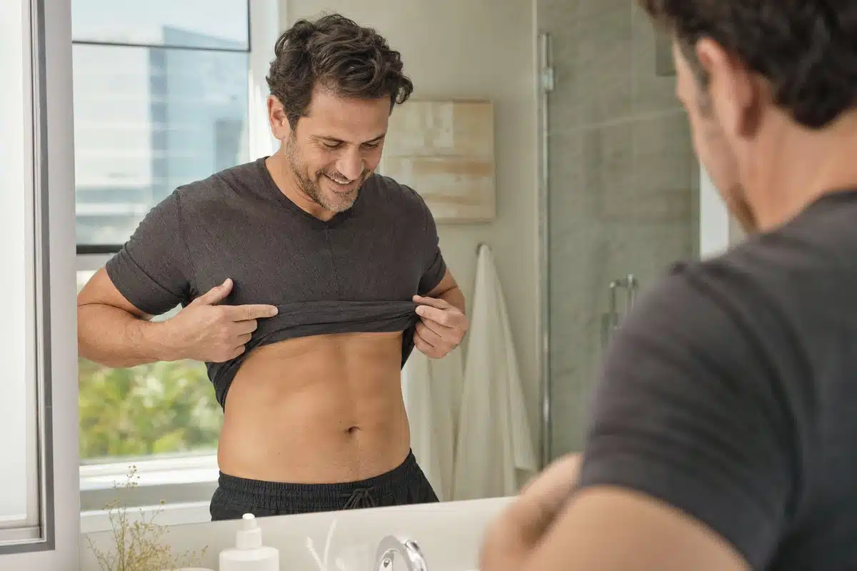 Man in his 40s admiring his slimmer midsection in a mirror after GLP-1 weight loss treatment
