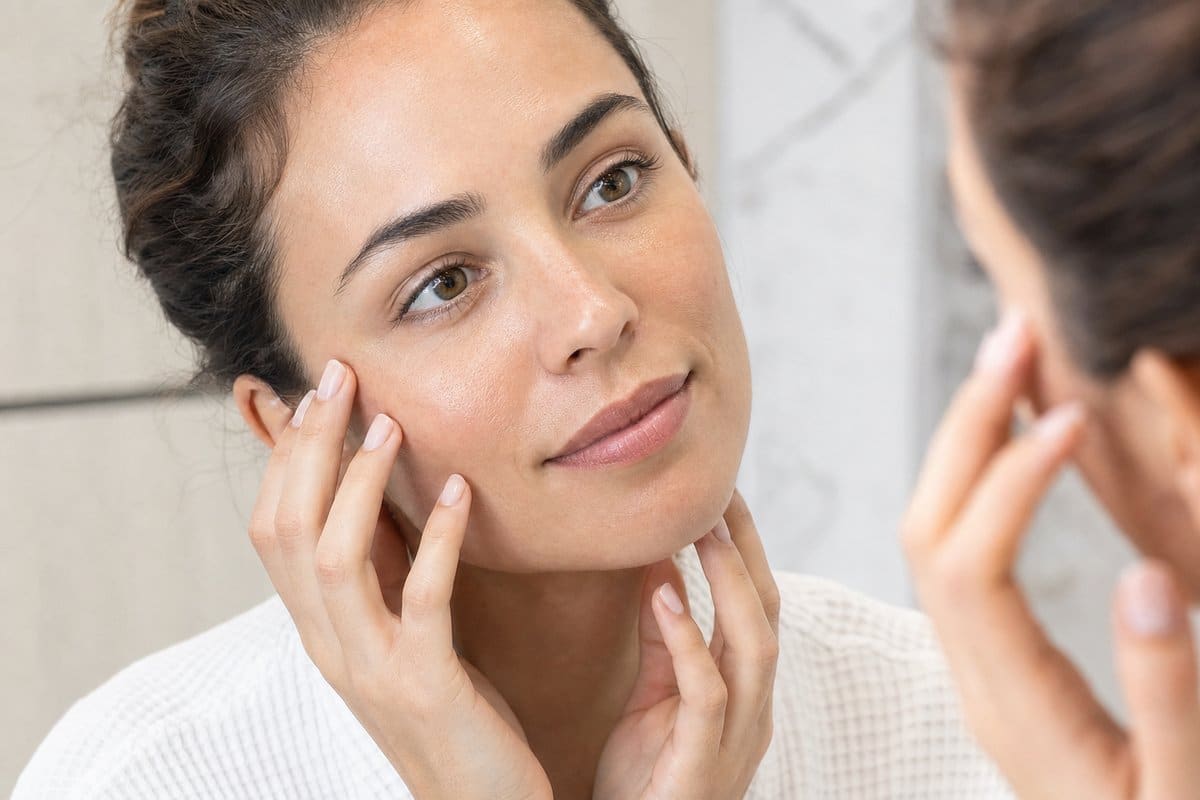 Young woman admiring her smooth, glowing facial skin in a mirror after platelet-rich plasma therapy at Miami Lakes Med Spa