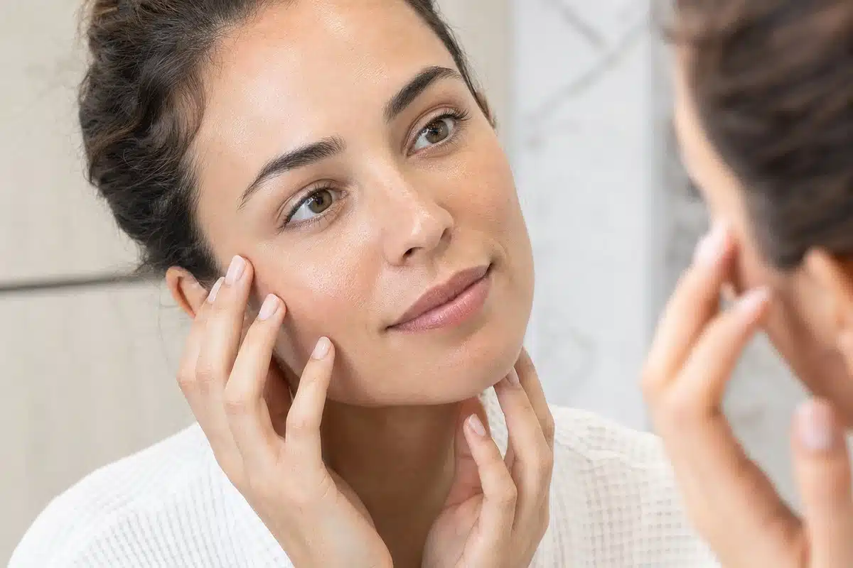 Young woman admiring her smooth, glowing facial skin in a mirror after platelet-rich plasma therapy at Miami Lakes Med Spa