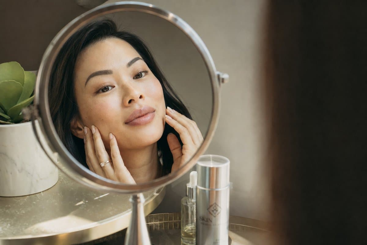Asian woman in her late 20s admiring natural full face filler results including balanced cheeks and lips in a mirror